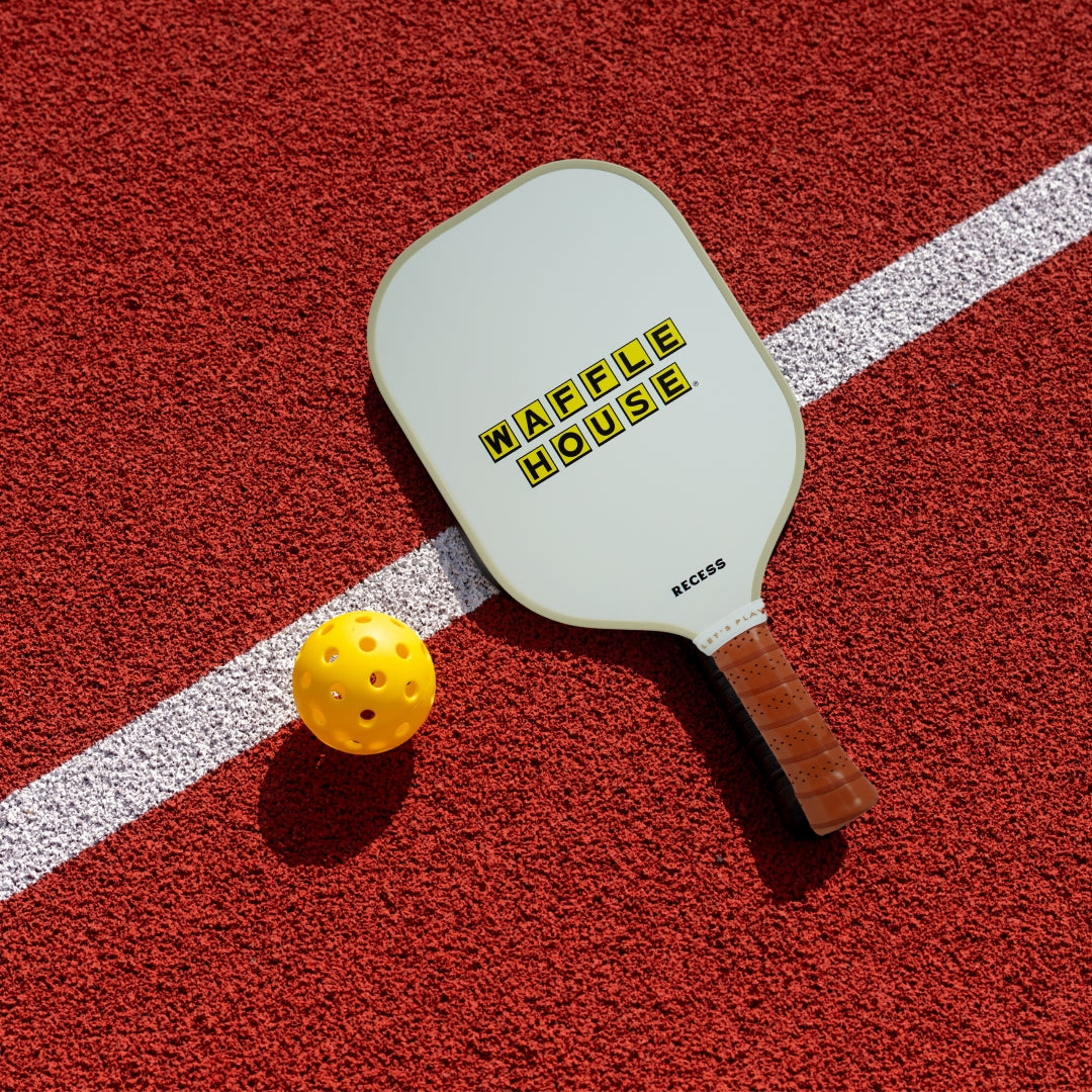 Waffle House pickle ball laying on a court with a pickle ball laying beside it