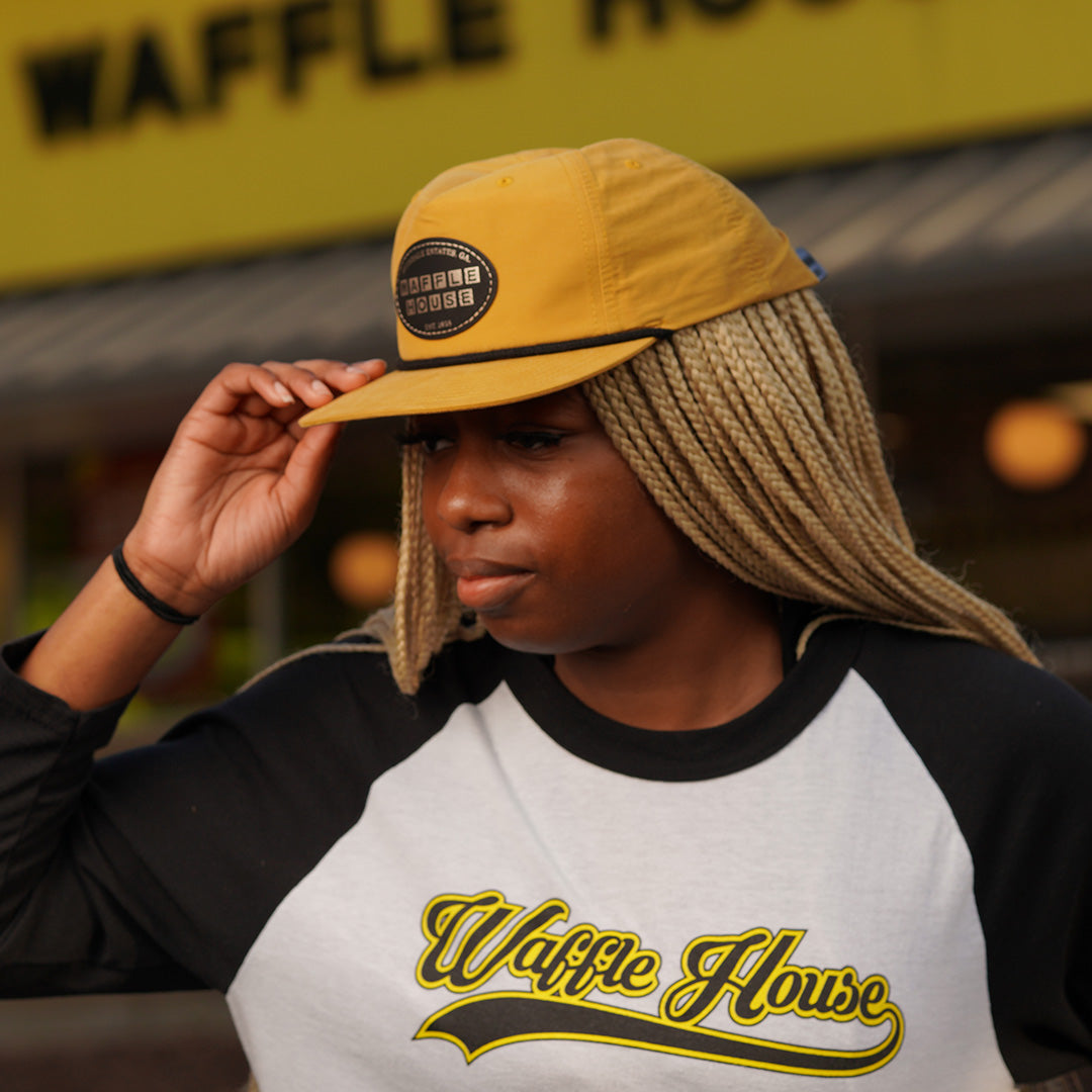 side image of woman wearing retro yellow Waffle House patch hat