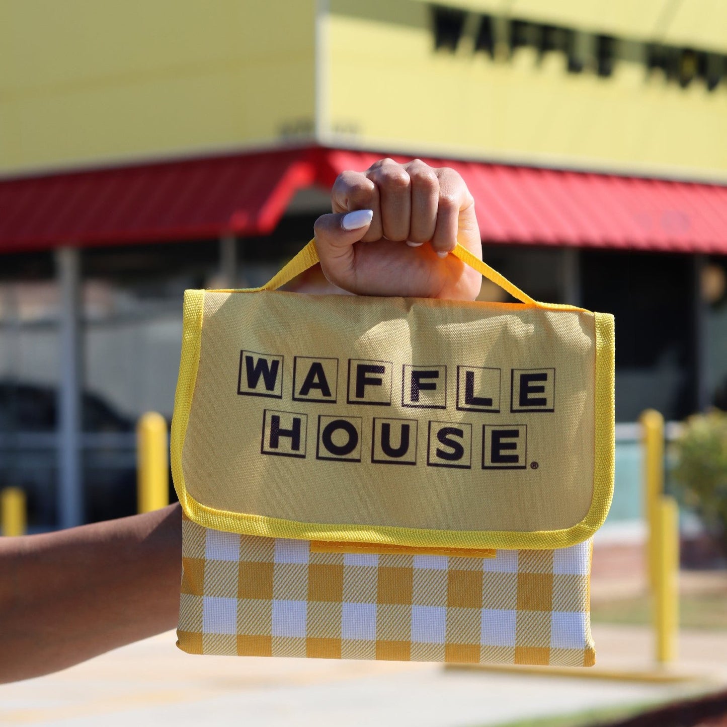 Yellow and white checked folded up blanket with Waffle House logo held up in front of Waffle House store