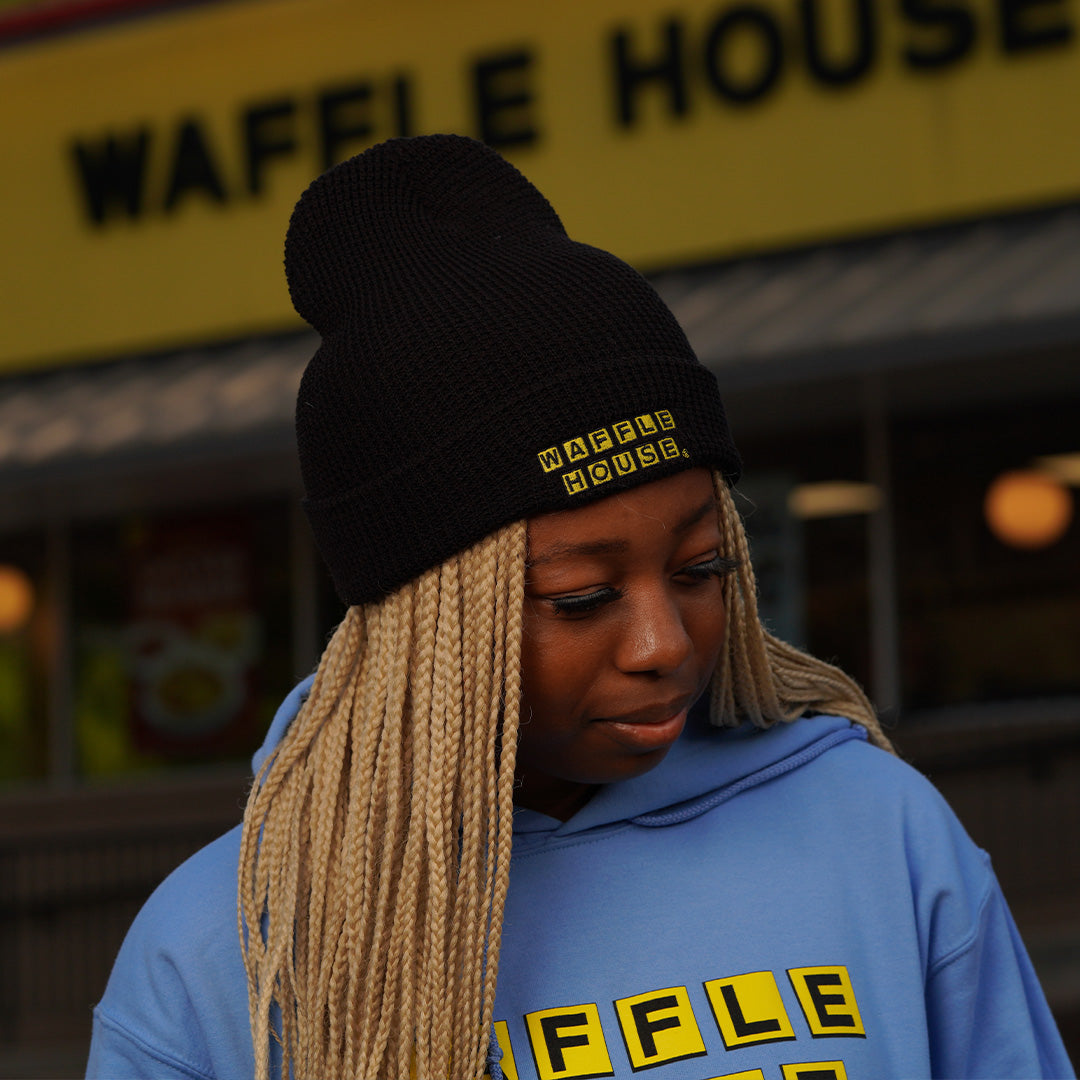 black beanie with Waffle House logo on front cuff being worn by woman standing in front of a Waffle House