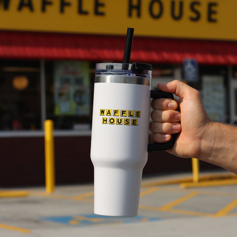 white tumbler with straw with Waffle House logo held by a hand in front of a Waffle House restaurant