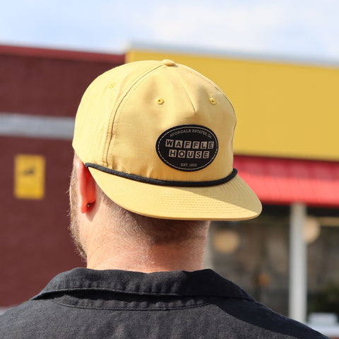 Man standing in front of Waffle House wearing a yellow hat backwards with Waffle House stiched patch.