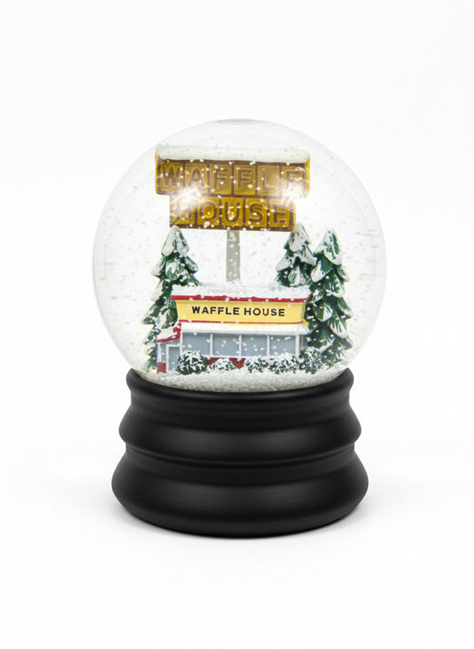 It’s a snow globe with a tiny Waffle House building and its tall yellow sign surrounded by snowy trees, all resting on a simple black base.