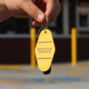 Yellow motel keychain with black Waffle House logo being held by a persons hand.