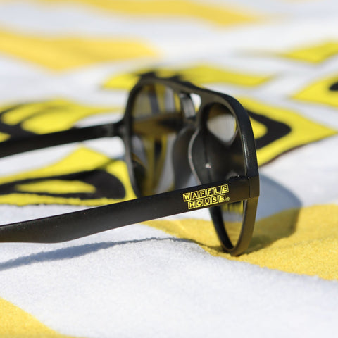 Black sunglasses with Waffle House logo on arm laid out on towel