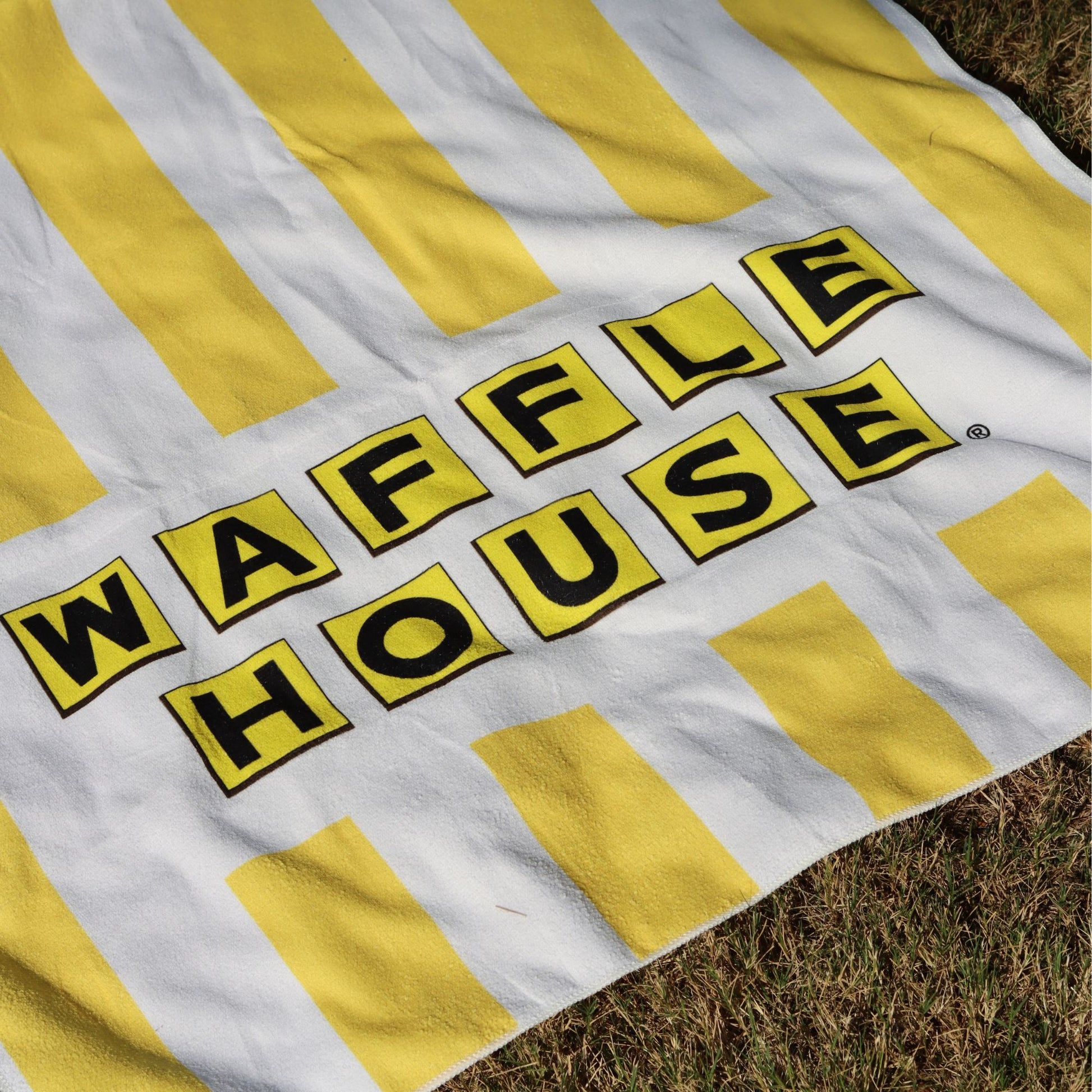 yellow and white striped beach towel with the waffle house logo laid out on grass