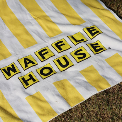 yellow and white striped beach towel with the waffle house logo laid out on grass