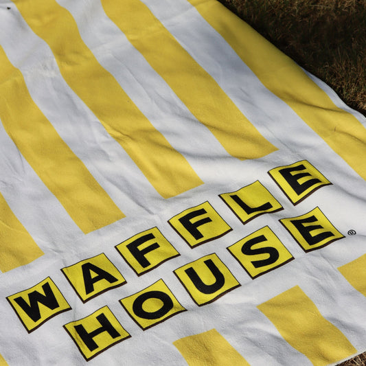 yellow and white striped beach towel with the waffle house logo laid out on grass