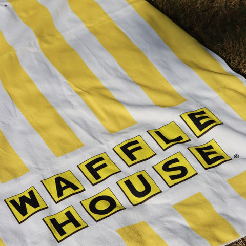 yellow and white striped beach towel with the waffle house logo laid out on grass