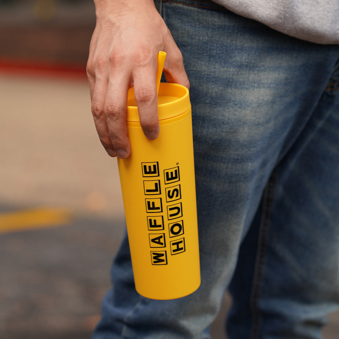 hand holding a yellow tumbler with straw and black Waffle House logo 