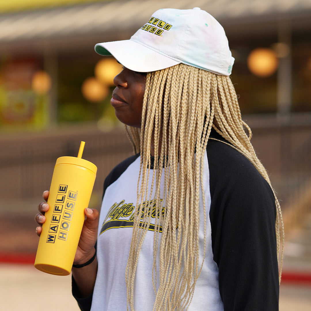 woman holding a yellow tumbler with straw and black Waffle House logo standing in front of a Waffle House