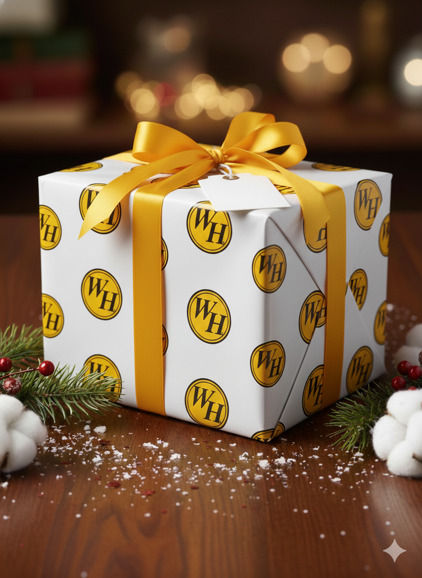 Gift wrapped in white paper with the circle WH logo repeating, finished with a big yellow ribbon and surrounded by festive winter décor.