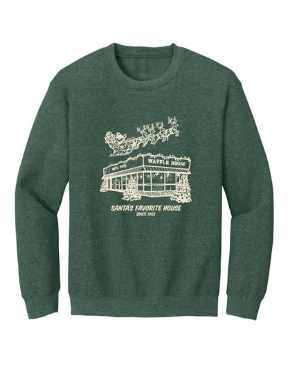 Green sweatshirt featuring a cream-colored drawing of a snowy Waffle House with Santa and his reindeer flying overhead, along with the words “Santa’s Favorite House Since 1955.