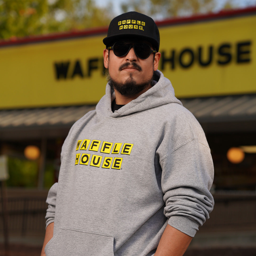 Man standing in front of a Waffle House wearing Grey Hoodie with yellow and black waffle house logo across the front