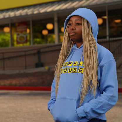 Woman wearing blue hoodie with yellow Waffle House logo on the front. She is standing in front of a Waffle House.