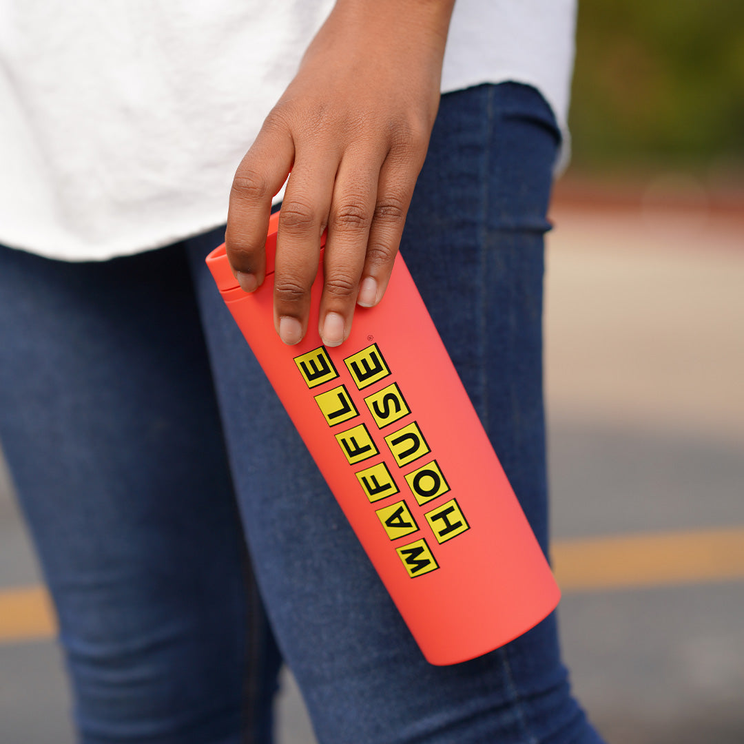 persons hand holding a melon colored tumbler with straw and black Waffle House logo 