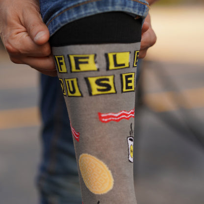 Person pulling up Waffle House dress socks onto their leg. Showing off Waffle House logo, waffles, bacon, coffee displayed on the socks.