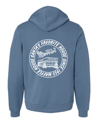 Blue hoodie featuring a large white circular design of Santa flying over a snowy Waffle House with the words “Santa’s Favorite House — Waffle House — Since 1955” wrapped around it.