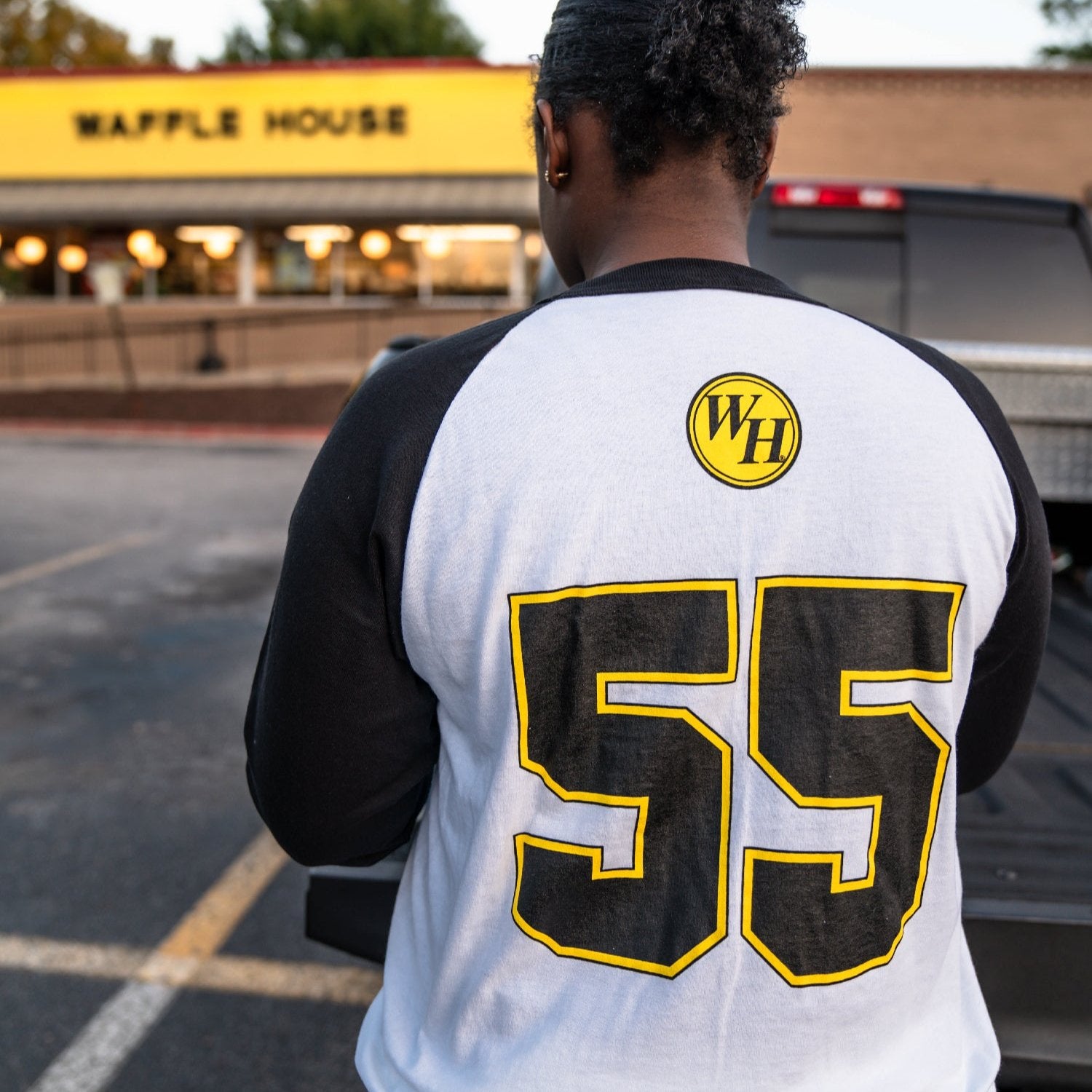 Back of woman standing in front of Waffle House wearing a shirt with a circle Waffle House logo and the number 55 on the back