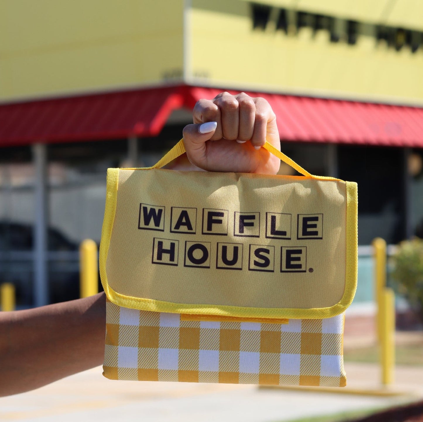 Yellow and white checked folded up blanket with Waffle House logo held up  in front of Waffle House store