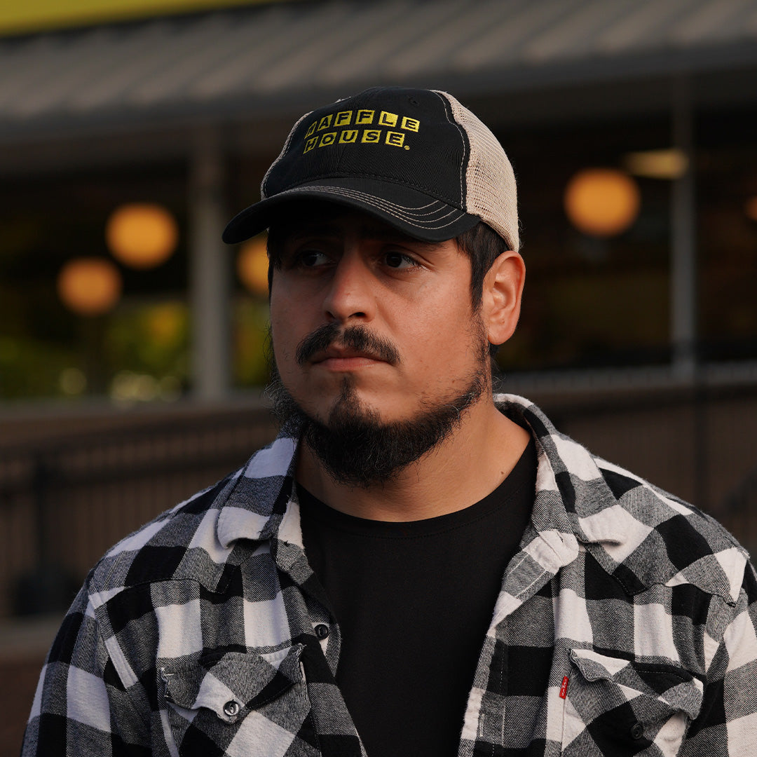 man in front of Waffle House wearing black trucker cap with yellow and black Waffle House logo and white mesh back.