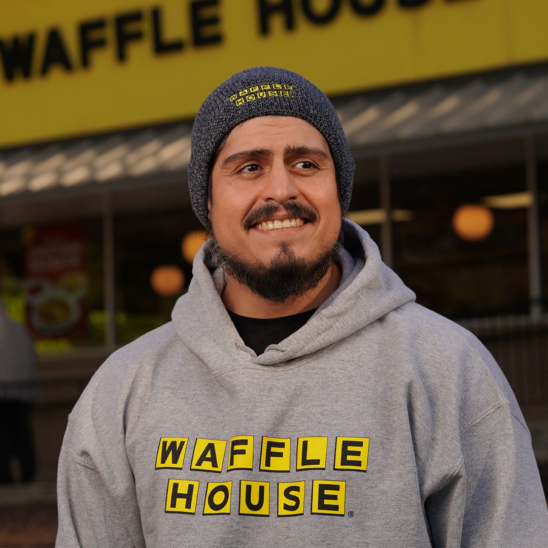 Navy marled knit beanie with the Waffle House logo being worn by a man standing in front of Waffle House