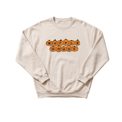 A cream (bone-colored) crewneck sweatshirt with long sleeves and ribbed cuffs and hem. On the chest, the words "Waffle" and "House" are spelled out in two rows using orange jack-o'-lantern pumpkins, each with a black carved letter and a green stem.