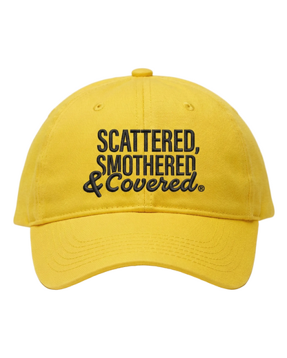 A bright yellow baseball cap with black embroidered text reading “Scattered, Smothered & Covered.”