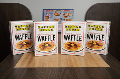 4 boxes of Waffle House waffle mix sitting on the table of a booth with a Waffle House menu in the background