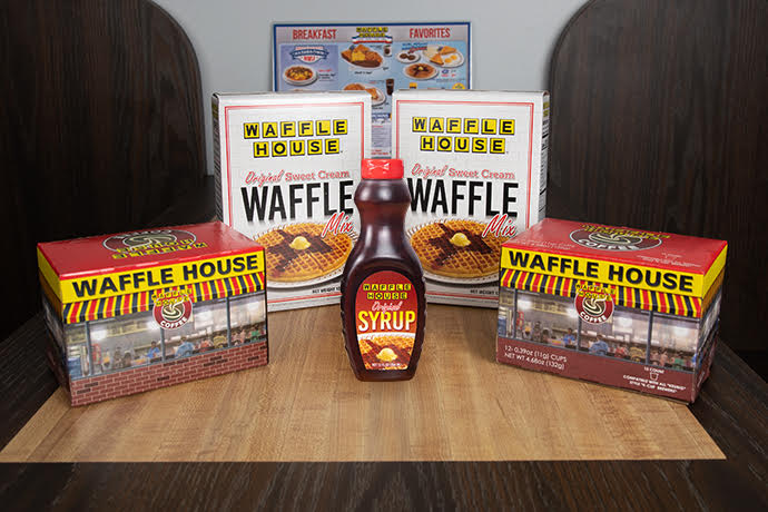 Two boxes of Waffle House waffle mix and two boxes of Waffle House Coffee single cup coffee pods and one bottle of Waffle House syrup on table.