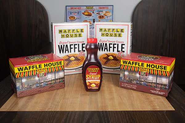 Two boxes of Waffle House waffle mix and two boxes of Waffle House Coffee single cup coffee pods and one bottle of Waffle House syrup on table.