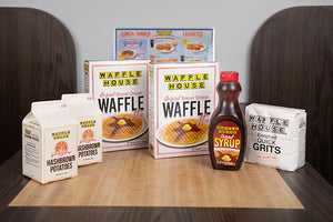 Two boxes of Waffle House waffle mix, two boxes of Waffle House hashbrowns, one pack of Waffle House grits and one bottle of Waffle House original syrup sitting on table of a booth